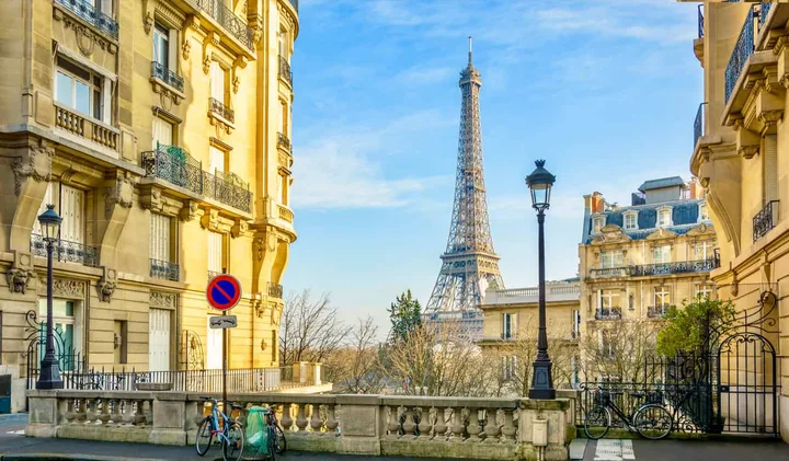 Sunny Paris street with Haussmann buildings, bicycles, and Eiffel Tower visible in background.