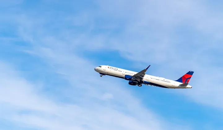 Delta Airlines passenger jet climbing through a blue sky with wispy clouds.