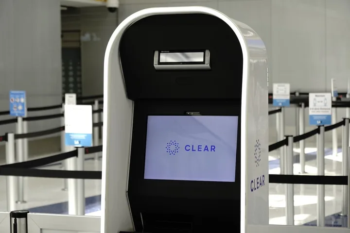 A CLEAR biometric kiosk with logo screen stands in an empty airport security lane.