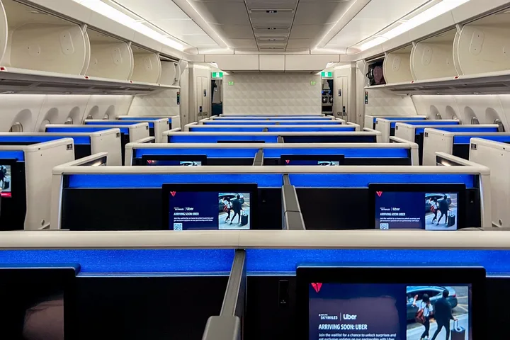 Empty Delta business class cabin with blue-lit lie-flat seats and seatback screens showing Delta SkyMiles promotion.