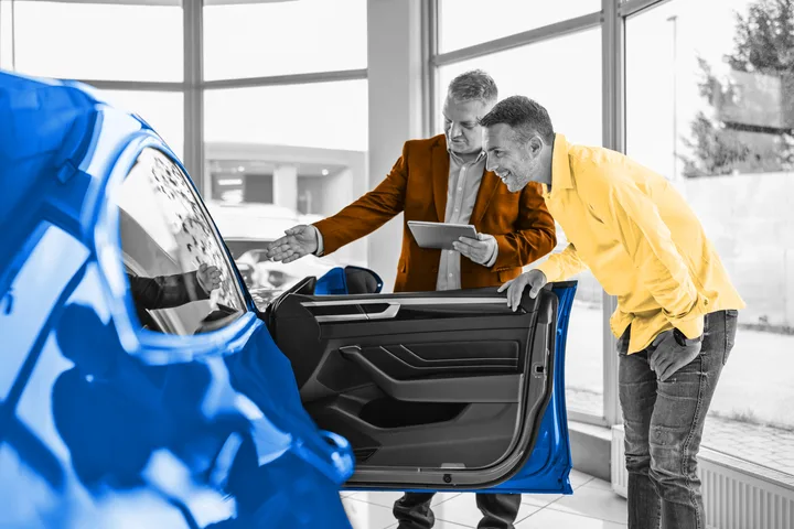 Car salesman with tablet showing a blue car interior to a smiling customer in a dealership showroom.