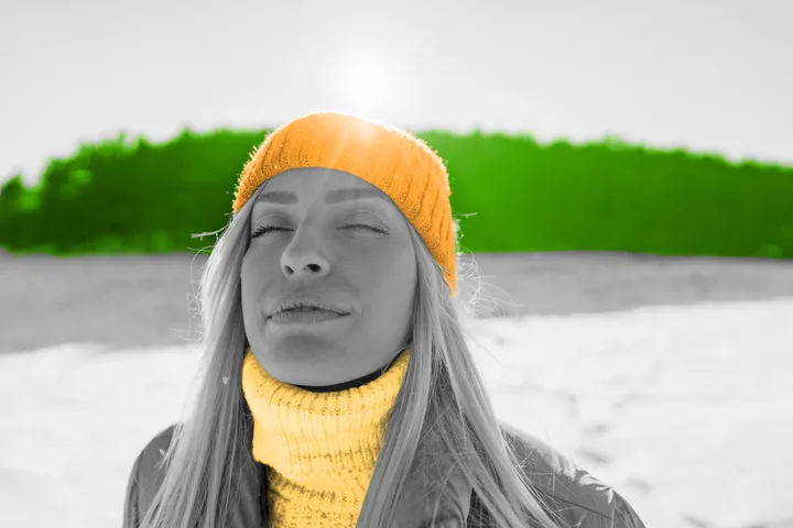 Woman in orange knit hat and scarf standing in snow with eyes closed, serene expression.