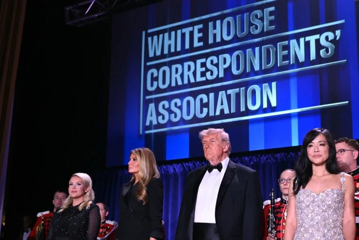 Several formally dressed people stand on stage in front of White House Correspondents' Association signage at a gala.