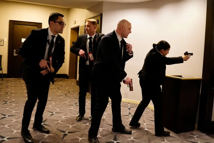 Four Secret Service agents with drawn weapons move through a hotel corridor in an active security response.