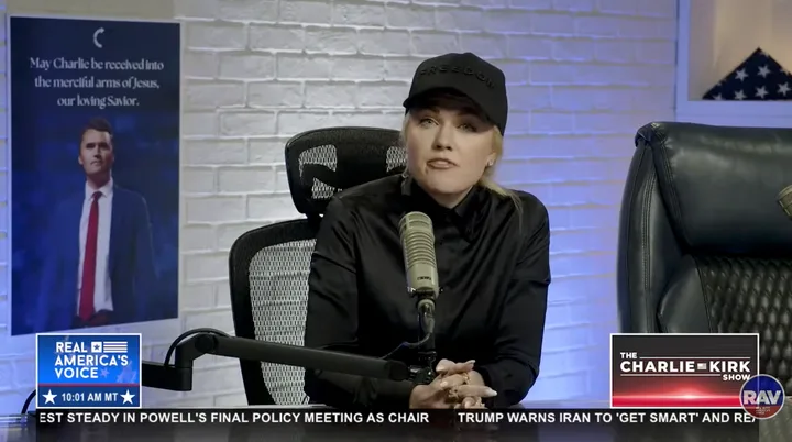 Erika Kirk in black outfit and cap speaks at microphone on The Charlie Kirk Show set.