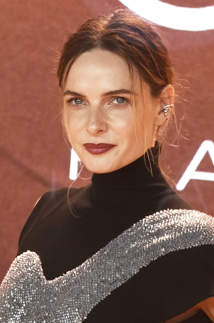 Dark-haired woman with blue eyes in elegant black turtleneck at a formal event or premiere.