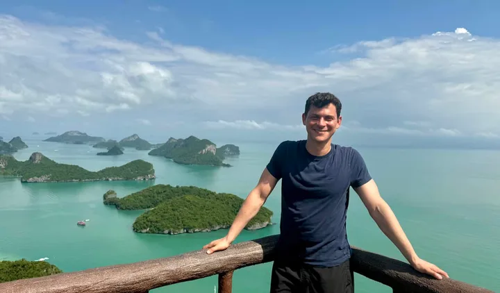 Smiling male traveler posing at viewpoint overlooking tropical island archipelago with turquoise sea.