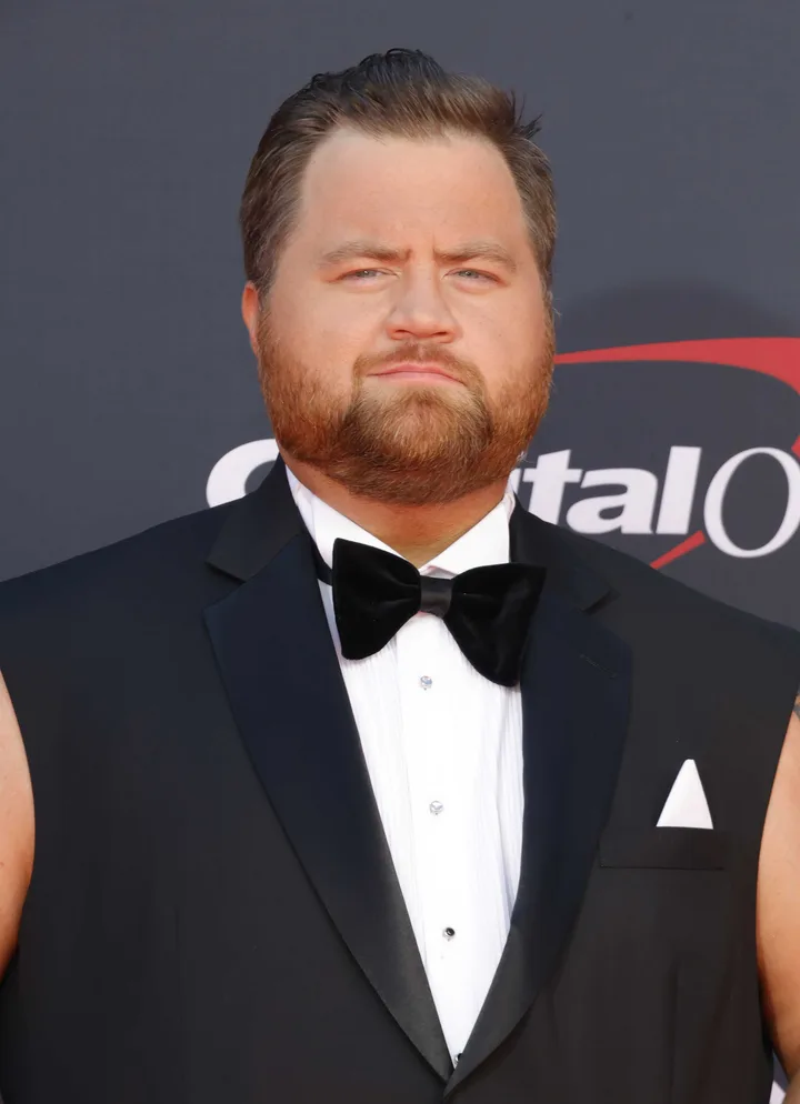 A heavyset man in a black tuxedo with bow tie posing at a formal red carpet event.
