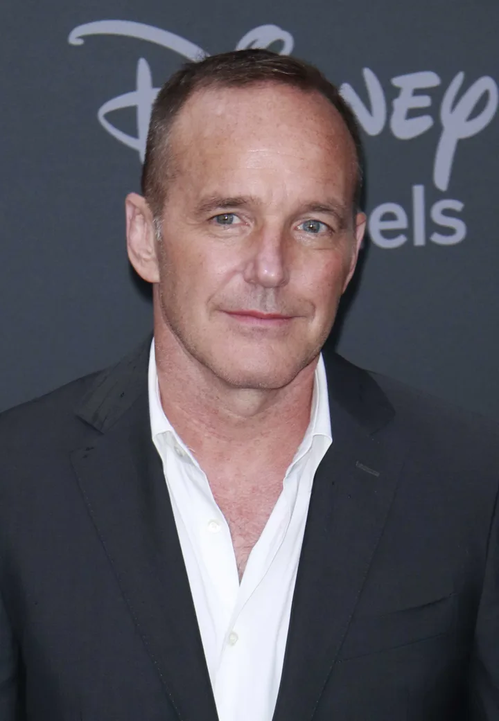 A middle-aged man in a dark blazer poses at a Disney event, smiling slightly.