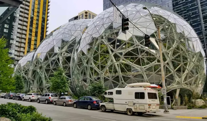 A vintage RV trailer parked on a city street in front of the Amazon Spheres in Seattle.