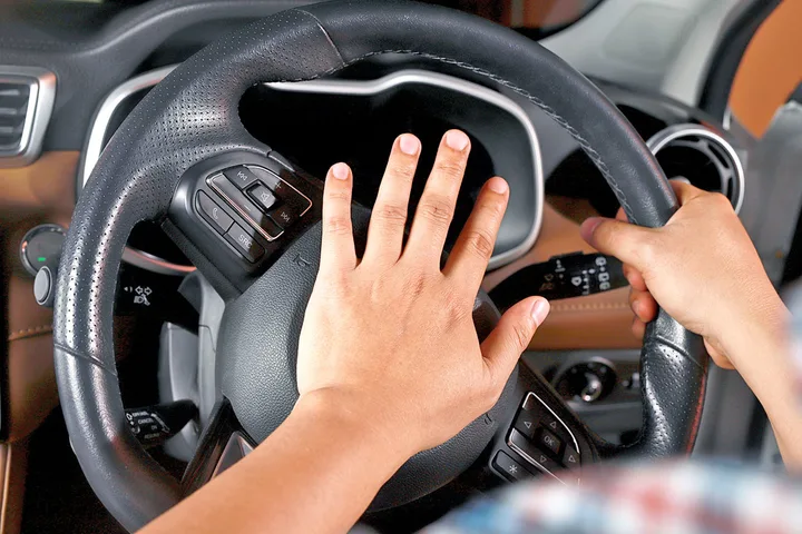 Close-up of hands pressing a car horn on a steering wheel.