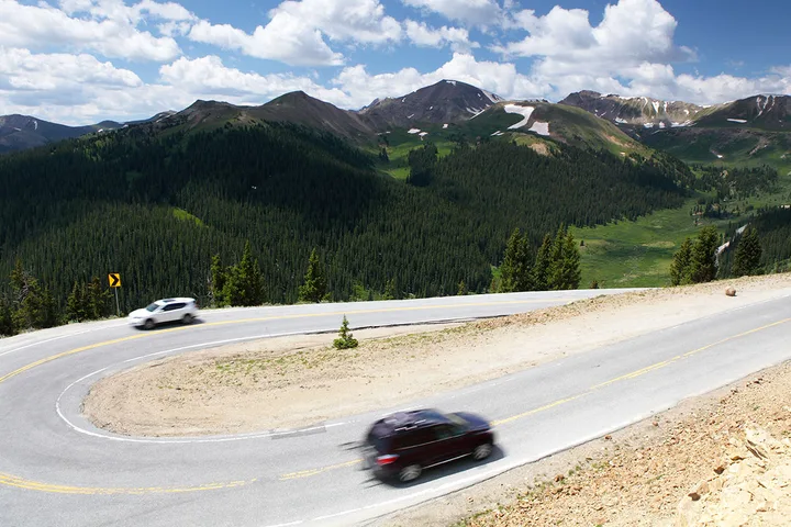 Two cars driving on a winding mountain road through a scenic alpine landscape.
