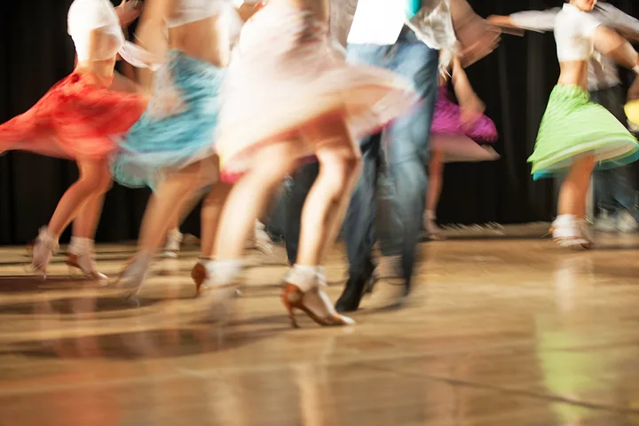 Colorful dancers in motion on a dance floor, skirts blurred from fast movement.