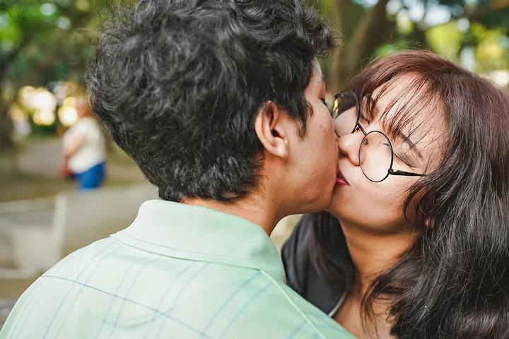 Young couple kissing outdoors in a park setting, close-up shot.
