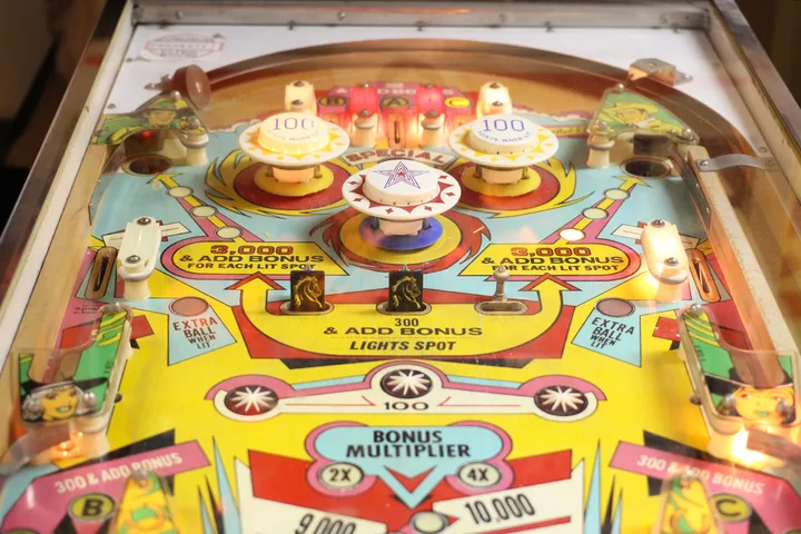 Close-up of a vintage colorful pinball machine playfield with bumpers and scoring labels.