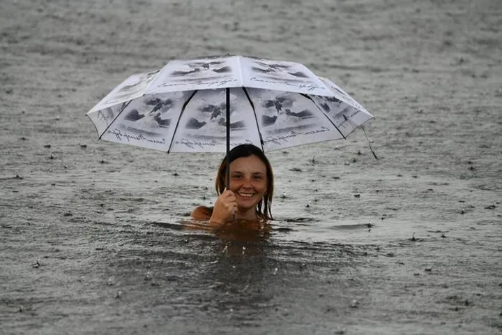 A smiling woman swimming in rain-soaked water while holding an open umbrella above her head.