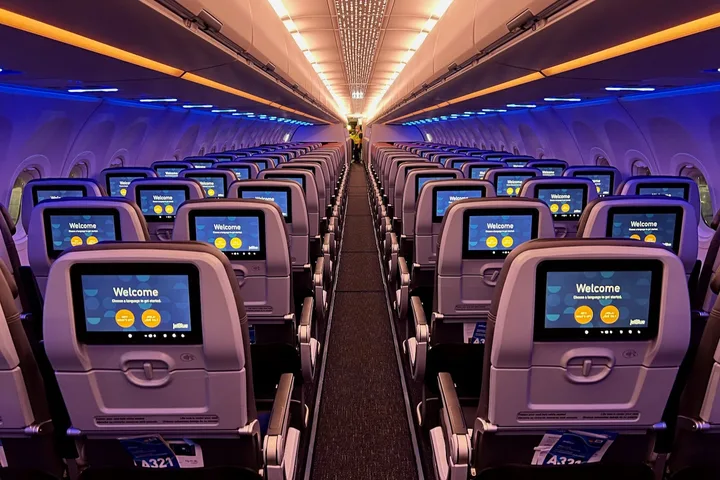 Empty JetBlue cabin interior with blue mood lighting and seatback screens displaying Welcome message.