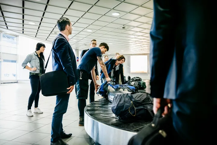 Travelers collecting luggage from baggage claim carousel at an airport.