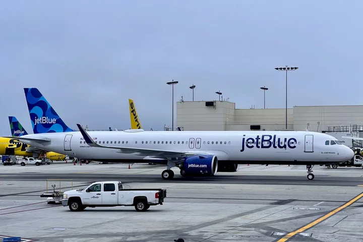 JetBlue aircraft parked at airport gate on overcast day with Spirit Airlines plane in background.