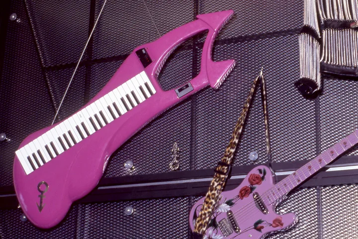 Purple keytar with Prince's symbol displayed on a wall alongside a pink guitar with a leopard-print strap.