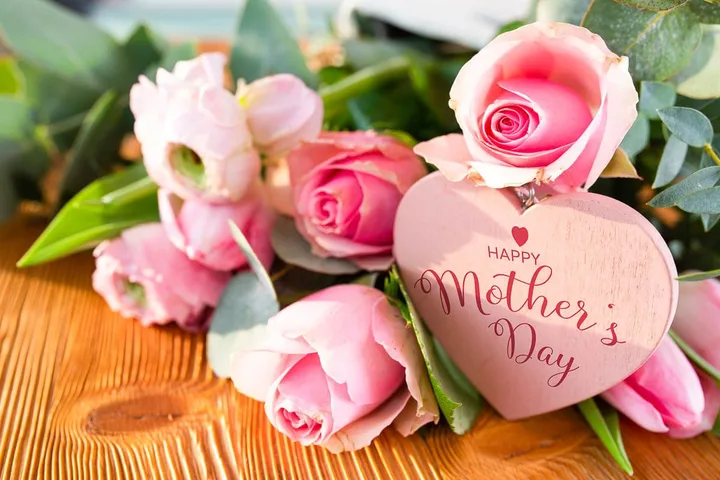 Pink roses and tulips arranged with a wooden heart tag reading 'Happy Mother's Day' on a wooden surface.