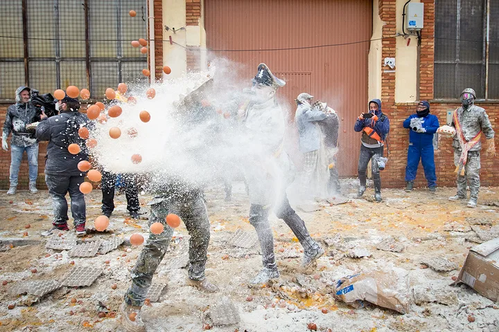 Chaotic outdoor egg-and-flour throwing festival with people covered in white powder.