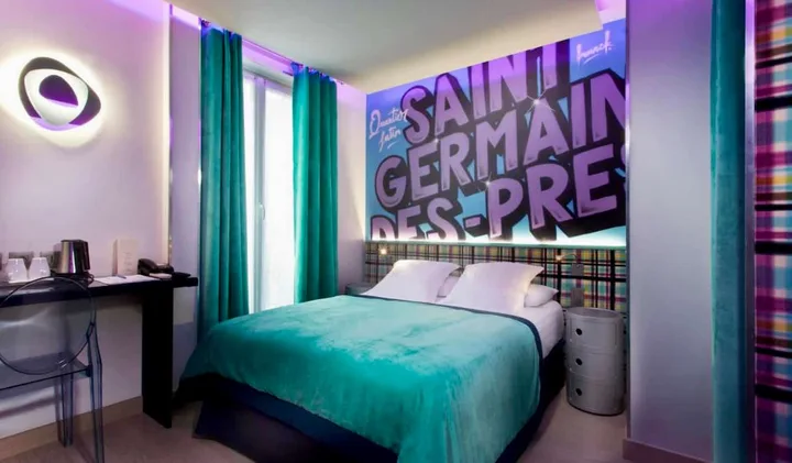 Vibrant hotel room with teal bedding and bold Saint-Germain-des-Prés mural as headboard wall art.