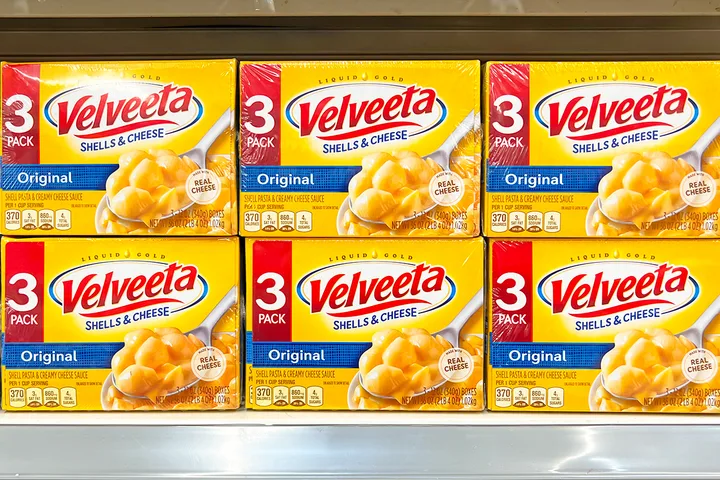 Six boxes of Velveeta Shells and Cheese stacked on a store shelf.