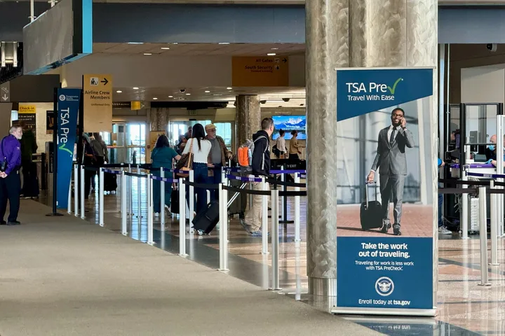 Airport security checkpoint with TSA PreCheck signage and travelers queuing.