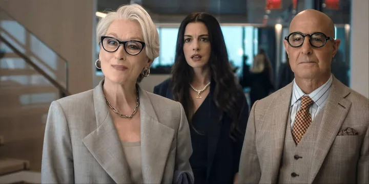 Three actors in elegant attire walk through a modern interior, looking serious and stylish.