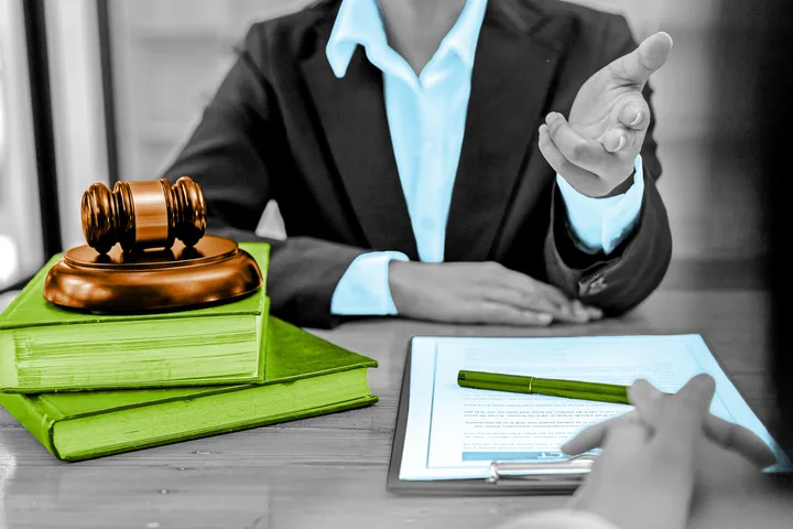 Lawyer at desk with gavel, legal books, and documents in a stylized color-highlighted photo.