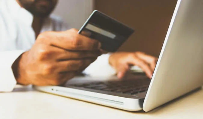 Person holding a credit card while typing on a laptop, warm-toned lifestyle shot.