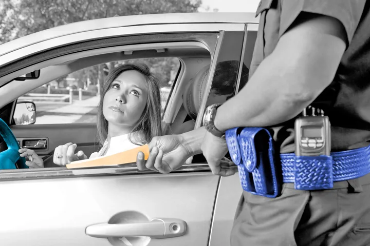 A police officer handing a traffic ticket to a woman sitting in a car window.